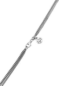 Silverfärgad kedjebröstband med en kräftklipp och en rund charm med genombruten design, tillverkad av hopkopplade metallringar.