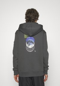 Sudadera con capucha de color gris oscuro que presenta un gran gráfico con un globo, la luna y texto en verde neón. Tela suave, capucha con cordón y puños acanalados.