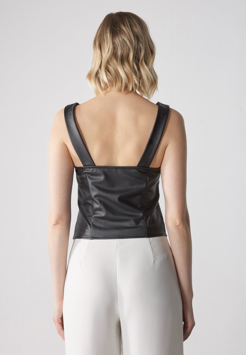 Top corto in ecopelle nera con spalline larghe, design aderente e superficie liscia. Il retro presenta un design scollato.