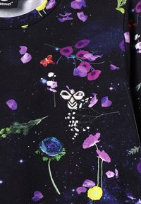 Svart tyg med blommönster i lila, rosa och blå färger; inkluderar broderad bi-detalj och en stjärnliknande bakgrundseffekt.