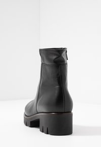 Bottine en cuir noir à bout rond, avec une fermeture éclair sur le côté, un tige texturée et un talon épais à crans. Fini lisse et détails de couture.