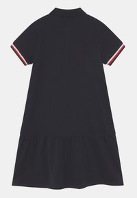 Námořnické modré polo šaty s krátkým rukávem, které mají červené a bílé akcenty na manžetách. Rozšířený lem s nařaseným volánem na spodním okraji.