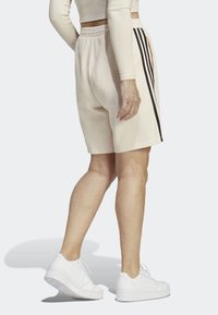 Beige ribbade shorts med elastisk midja, prydda med svarta sidostråk. Kombineras med vita sneakers som visar en texturerad tyg.