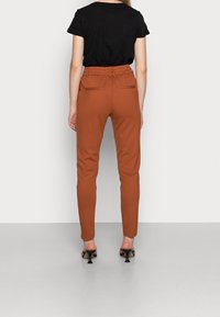 Bruna slim-fit byxor med elastisk midja, bakfickor och avsmalnande ben, kombinerade med en svart topp med kort ärm.