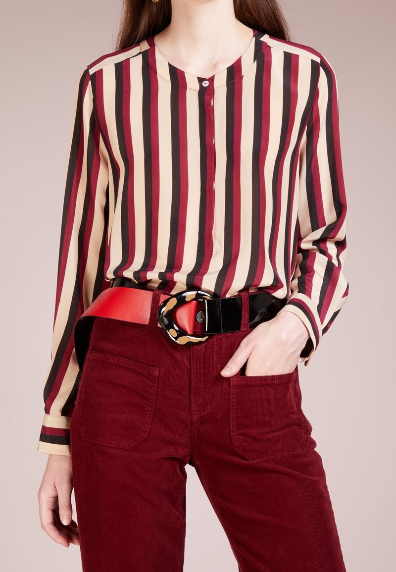 Blouse rayée en beige, rouge et noir ; fermeture à boutons. À associer avec un pantalon en velours côtelé bordeaux et une large ceinture noire avec une boucle à motif.