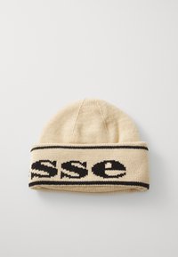 Strikket lue i beige med en svart remsa som har tekst. Har en brettet kant og en sømløs krone, glatt tekstur. Enkel design.
