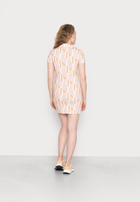 Vestido de manga curta em rosa claro com riscas diagonais em laranja e branco, apresenta um colarinho e uma silhueta ajustada, combinado com ténis laranja.