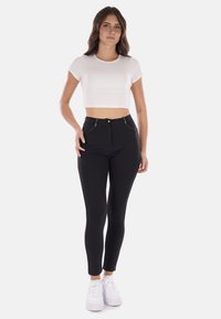 Jeans skinny neri a vita alta con tasche frontali, chiusura a pulsante in metallo e zip. Abbinati a una t-shirt cropped bianca e sneakers bianche.