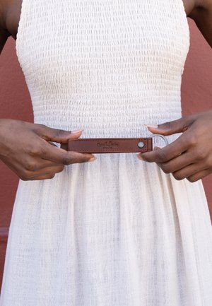 Person iført en hvid tekstureret ærmeløs kjole, der holder en brun lædernøglering med en metalring i taljehøjde.