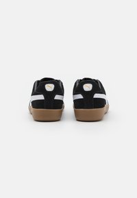 Schwarze Wildleder-Sneaker mit weißen Akzenten, rundem Logo und Gummisohlen, im lässigen Design und mit strukturierten Details.