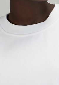 Felpa bianca con scollo rotondo e tessuto testurizzato, con un focus sul materiale liscio e sul design pulito.