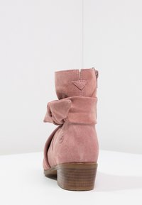Bottine en suede rose avec un détail de nœud, petit talon empilé, fermeture éclair à l'arrière et design à bout arrondi.