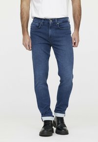 Slim-fit blauwe denim jeans met een klassiek vijf-pocket ontwerp, omgeslagen bij de enkels, en gecombineerd met zwarte veterschoenen.