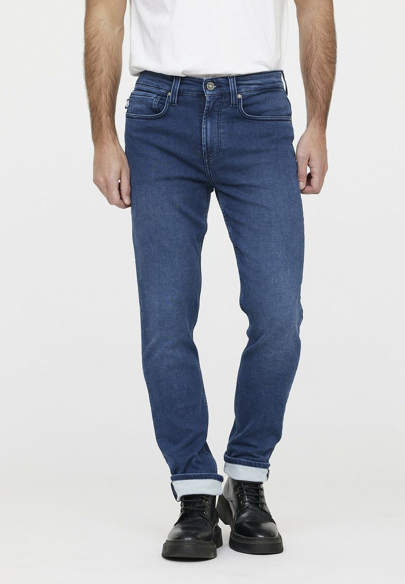 Slim-fit blauwe denim jeans met een klassiek vijf-pocket ontwerp, omgeslagen bij de enkels, en gecombineerd met zwarte veterschoenen.