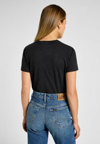 T-shirt nera a maniche corte abbinata a jeans blu in denim a vita alta, con un patch in pelle con logo in vita e tasche posteriori cucite.