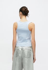 Ανοιχτό μπλε ριγωτό τοπ με στρογγυλή λαιμόκοψη και φαρδιές μασχάλες, συνδυασμένο με ασημένιο μεταλλικό παντελόνι φαρδι άς γραμμής.