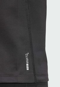 Schwarzes Thermaloberteil mit einer Rautentextur, das ein kleines weißes "CLIMAWARM"-Logo in der unteren rechten Ecke und Flachnähte entlang der Nähte aufweist.