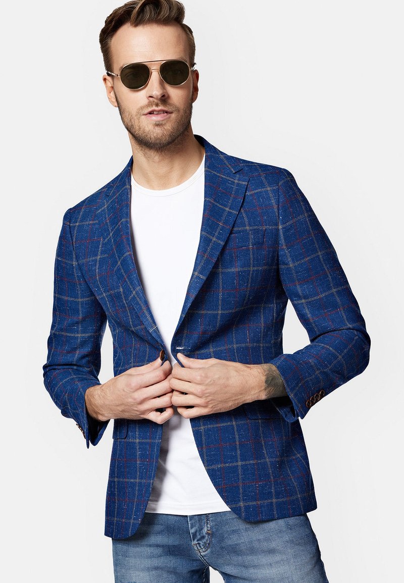 Niebieska marynarka w kratę z teksturowanej tkaniny, z klapami w kształcie litery notch i zapięciem na jeden guzik. Połączona z białym t-shirtem i niebieskimi dżinsami.