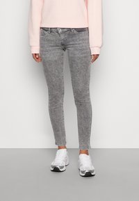 Jeans skinny grigi con un lavaggio sbiadito, vita media e dettagli di cucitura sottili, abbinati a scarpe da ginnastica bianche.