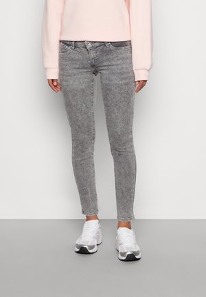 Grijze skinny jeans met een vervaagde wassing, middelhooge taille en subtiele stikseldetails, gecombineerd met witte sportschoenen.