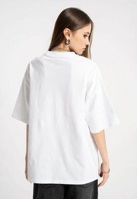 Biała, oversize'owa koszulka z krótkim rękawem, wykonana z bawełny. Posiada okrągły dekolt i gładką teksturę, bez widocznych wzorów czy grafik.