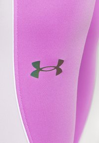 Detailní záběr růžové atletické tkaniny s černým logem Under Armour a bílým lemováním po okraji.