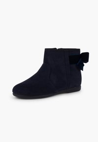 Stivale alla caviglia in suede blu navy con una texture liscia e punta arrotondata. Presenta una suola in gomma e un fiocco laterale con una fascia elastica per i dettagli.