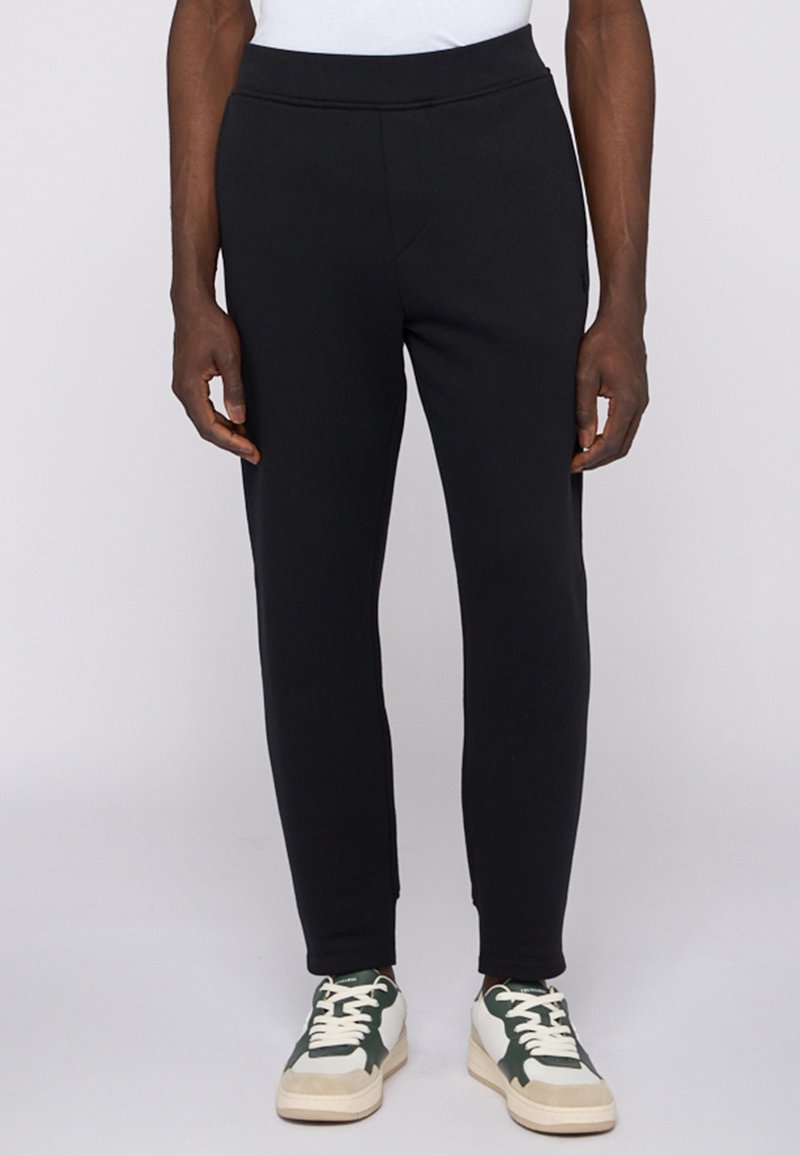 Svarta sweatpants med en smal passform, mjukt material, elastisk midja och sidofickor, kombinerat med gröna och vita sneakers.