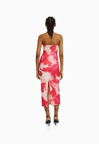 Robe midi sans manches présentant un motif tie-dye rose et blanc, au design ajusté avec une fente, fabriquée en tissu extensible pour une silhouette moulante.
