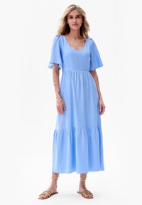 Jasnoniebieska sukienka maxi z krótkimi falbaniastymi rękawami, dekoltem w serek, dopasowanym toplinem oraz warstwowym, falbaniastym dołem. Gładka, lekka tekstura materiału.
