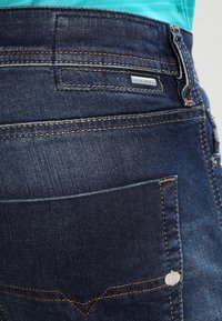 Mörkblå denimjeans med synliga sömmar och en liten märkesetikett. Har en blekt struktur och en design för bakfickan.