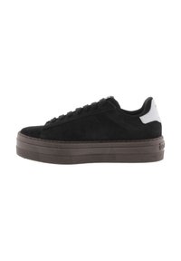 Zapatilla de ante negra con una suela de goma marrón gruesa, puntera redondeada y diseño de cordones. Presenta un acento en el talón en blanco contrastante.