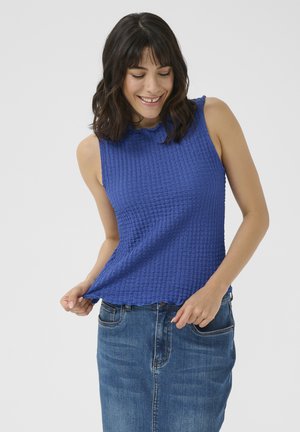 Plava bezrukava majica sa teksturiranim, valovitom tkaninom i valovitim rubom. Uparena s traper suknjom, prikazuje ležeran stil.