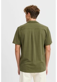 Camisa de manga corta de color verde oliva con diseño de cuello. Presenta una costura horizontal en la parte posterior y un corte relajado. Fabricada con un tejido suave y texturizado.