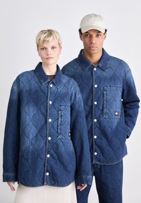 Quilted denimjakker i mørkeblå med trykknapper, med brystlommer og en merkevarelogo på lommen til herrejakken.