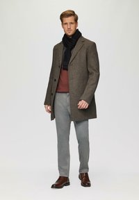 Brauner Fischgrätmantel, schwarzer Schal, kastanienfarbenes Oberteil, graue Hose und braune Schnürschuhe. Glatte Textur und taillierte Passform.