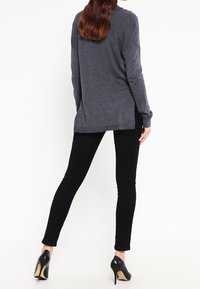 Mörkgrå långärmad tröja med avslappnad passform, sidslitsar och nederkanter med ribbad struktur, i kombination med svarta skinny jeans och svarta klackar.