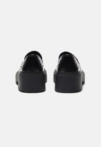 Chaussures à plateforme noires avec une tige en cuir lisse, présentant des dos arrondis, des semelles épaisses et des clous décoratifs sur les côtés.