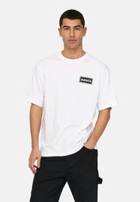 White cotton t-shirt with short sleeves and a round neck, featuring a black rectangular "oasis" logo on the left chest area.