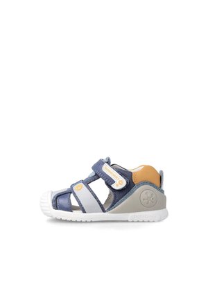 Sandalia en color marino y gris con tira de Velcro, diseño abierto, suela de goma y acento naranja en el talón. Parte superior texturizada para transpirabilidad.