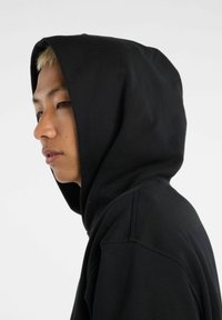 Sudadera negra con un corte relajado, tejido texturizado y una gran capucha. Presenta detalles de costura visibles y un diseño minimalista.