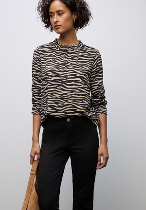 Blouse à manches longues et col côtelé, arborant un imprimé zèbre beige et noir. Associée à un pantalon noir ajusté et portant un sac marron clair.