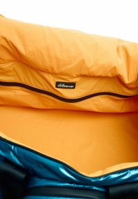 Interieur van een blauwe en oranje sporttas, met een gladde oranje voering, een bruine rits en een zwart label met logo nabij de opening.