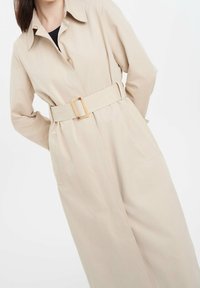 Beige trenchcoat med knytband i midjan, som har en krageskärning, knappar och sidofickor. Slätt, lätt material.