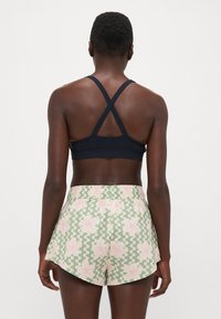 Black sports bra with crisscross straps, paired with green shorts featuring a floral pattern and wavy design, elastic waistband, and relaxed fit.