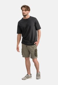 Zwarte t-shirt met korte mouwen, olijfgroene cargoshorts met zakken, en grijze sneakers. De stof lijkt zacht te zijn met een relaxte pasvorm.