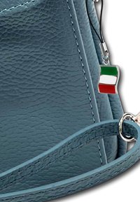 Blauwe leren handtas met textuur en een zilveren hardware accent, met een charm van de Italiaanse vlag bevestigd aan een zwarte strap.