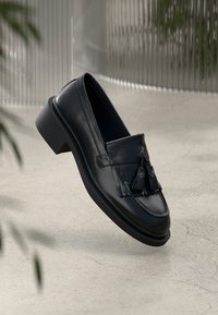 Mustat nahkakengät, joissa on tupsuakkentit, pyöreä kärki ja matala lohko korko. Sujuva pinta, jossa on selvät ompeluyksityiskohdat.