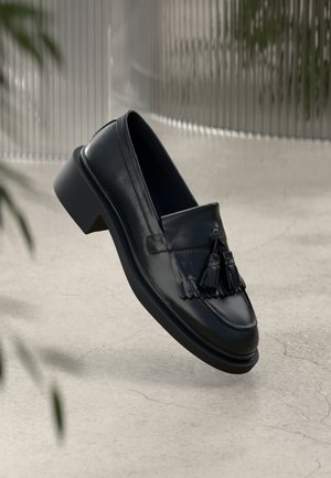 Mustad nahast loafers, kus on kaunistused frantsiisiaktsentidega, ümar varvas ja madal plokk-kreen. Sile tekstuur koos silmapaistvate õmbluste detailidega.