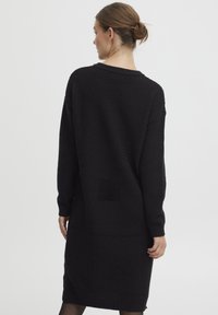 Vestito nero in maglia con un motivo testurizzato, maniche lunghe e una vestibilità morbida. Presenta una tasca posteriore applicata e polsini a costine.